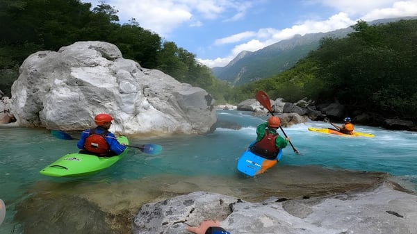 Schüler von Coláiste Naomh Cormac paddeln in bunten Kanus auf einem Fluss mit grüner Umgebung und felsigen Klippen.