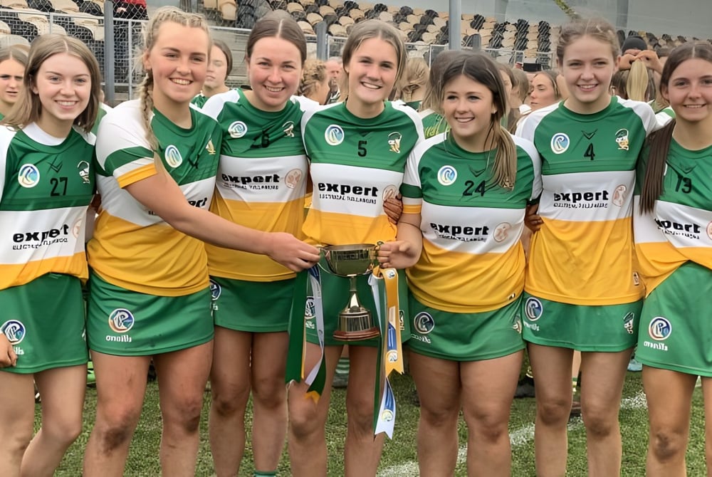 Schüler der Coláiste Naomh Cormac feiern im Stadion gemeinsam mit einem Pokal in der Hand.