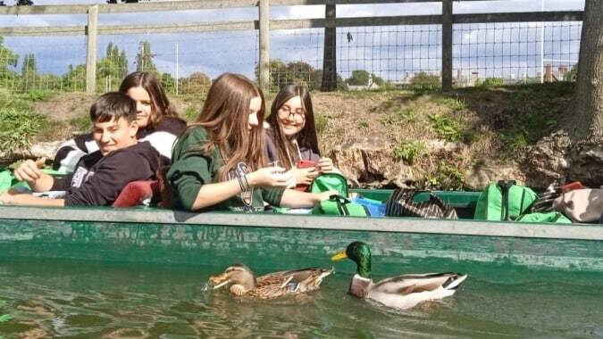 Eine Gruppe Schüler sitzt auf einer grünen Bank und beobachtet Enten in einem Teich auf dem Gelände des Colegio Argantonio.