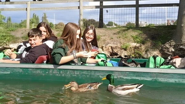Schüler der Colegio Argantonio sitzen auf einer Bank und blicken auf einen Teich mit schwimmenden Enten in ländlicher Umgebung.