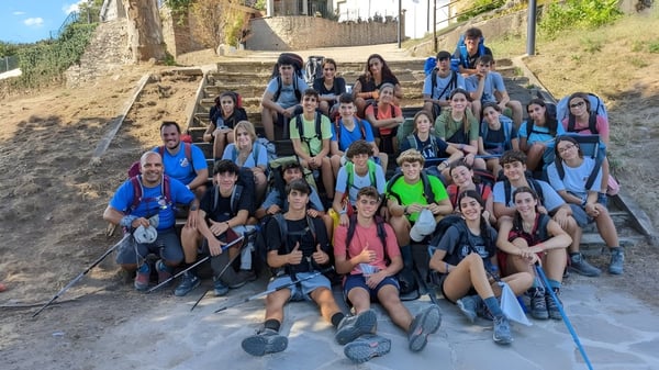 Eine Gruppe von Schülerinnen und Schülern sitzt auf den Außentreppen auf dem Campus des Colegio Esclavas vor Steinmauern und Grünflächen.