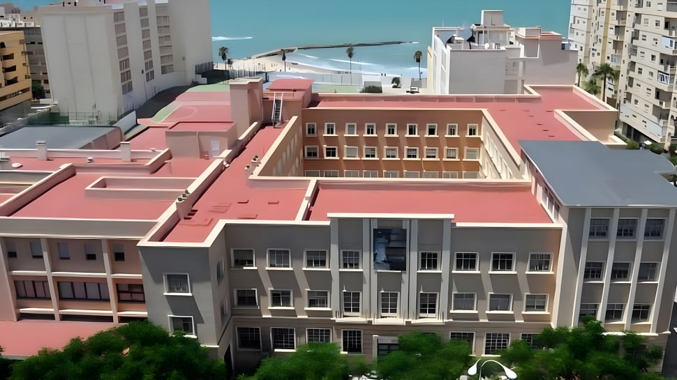 Das mehrstöckige pinkfarbene Gebäude des Colegio Esclavas steht vor einer städtischen Kulisse unter blauem Himmel.