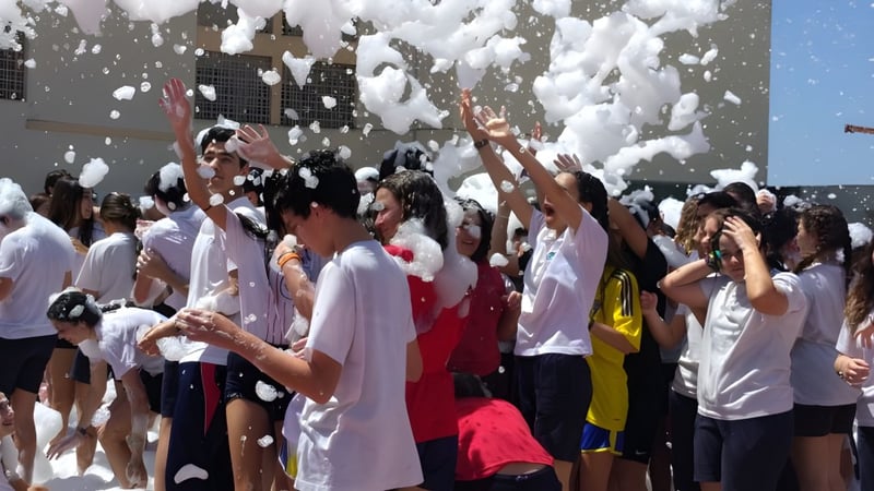 Eine Gruppe von Schülerinnen und Schülern in weißer Kleidung steht im Schnee vor Gebäuden auf dem Gelände des Colegio Esclavas.