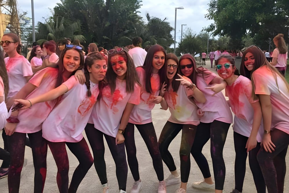 Eine Gruppe Schülerinnen des Colegio Esclavas posiert lachend im Freien vor Bäumen und Gebäuden.