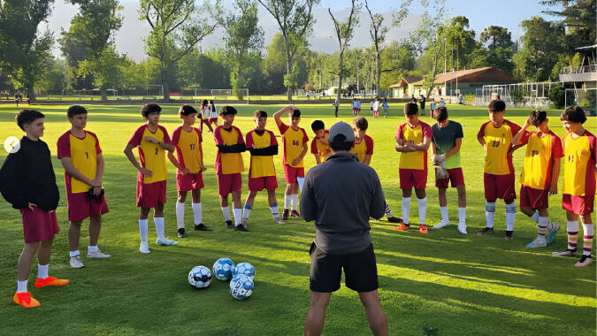 Eine Gruppe junger Fußballspieler steht beim Training auf dem Rasenfeld des Colegio San Gabriel mit einem Trainer vor ihnen.