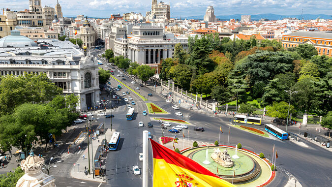 Eine lebendige Stadtansicht mit einer spanischen Flagge vor dem Colegio San Gabriel unter blauem Himmel.