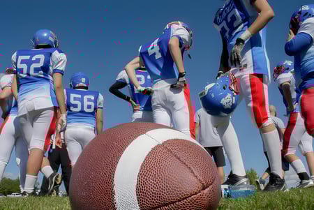 Eine Gruppe von Footballspielern der Collège Churchill High School steht in blauen und weißen Trikots auf dem Rasenfeld mit einem Football im Vordergrund.