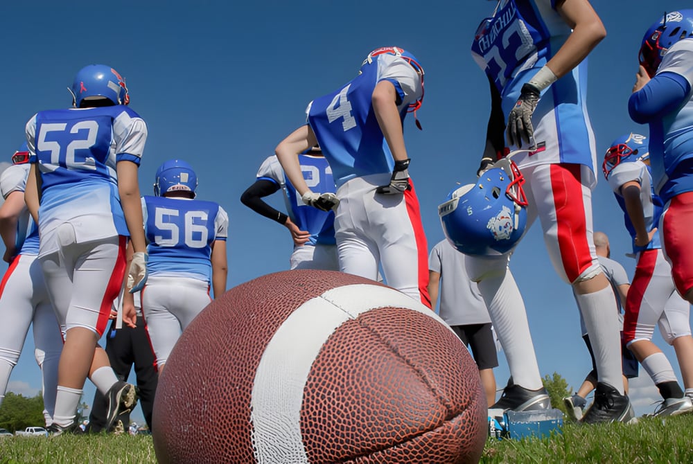 Eine Gruppe von Footballspielern der Collège Churchill High School steht in blauen und weißen Trikots auf dem Rasenfeld mit einem Football im Vordergrund.