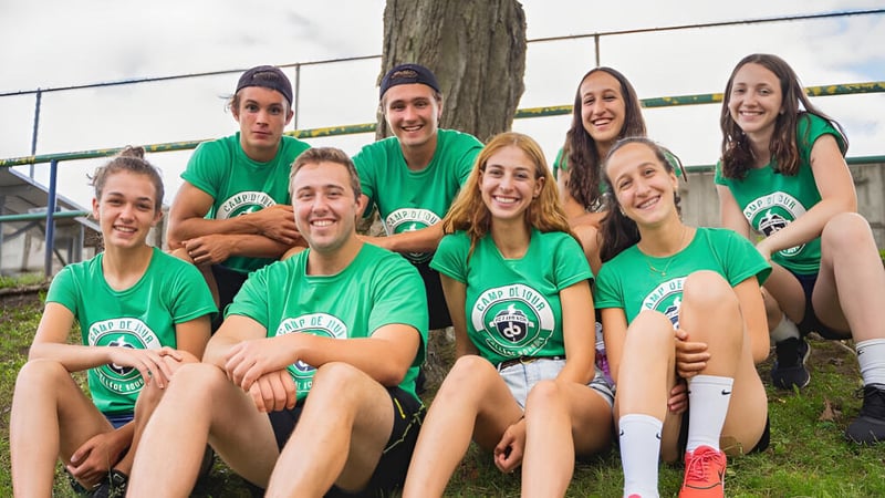 Eine Gruppe Schülerinnen und Schüler des College Bourget sitzt im Freien zusammen und lächelt vor einem hölzernen Hintergrund.