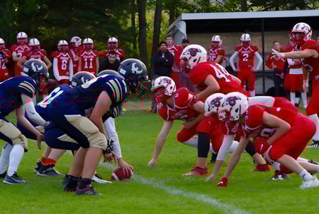 Schüler des Collège de Sainte-Anne-de-la-Pocatière spielen ein Fußballspiel auf dem Sportplatz mit Bäumen im Hintergrund.