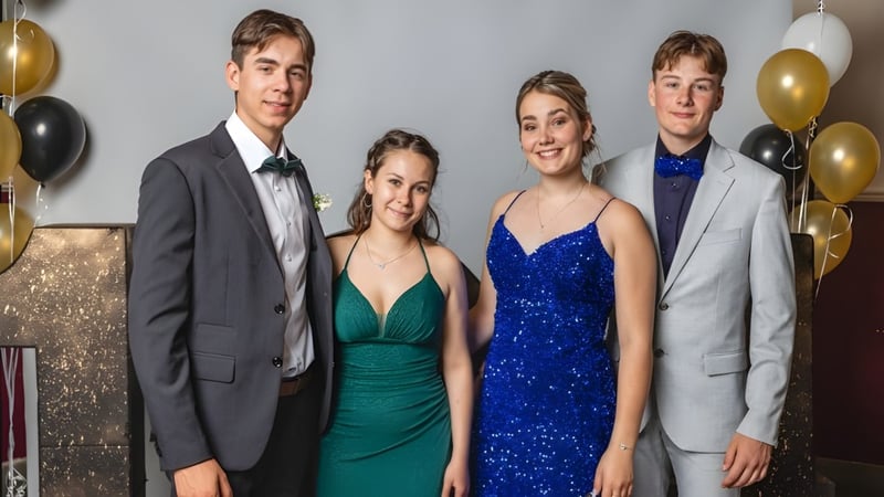 Vier Studierende des Collège de Sainte-Anne-de-la-Pocatière posieren formell vor einer ballonbesetzten glitzernden Wand.