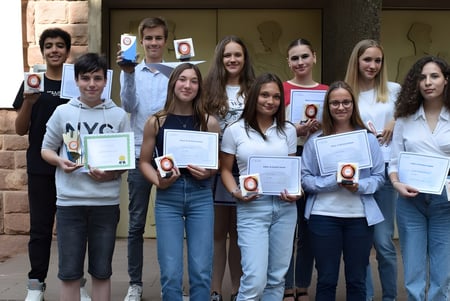 Schüler der Collège Episcopal Saint Étienne halten Auszeichnungen vor einem Backsteingebäude.