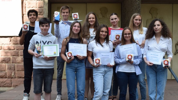 Eine Gruppe Schüler hält auf dem Hof des Collège Episcopal Saint Étienne gemeinsam Urkunden vor einer Backsteinmauer hoch.