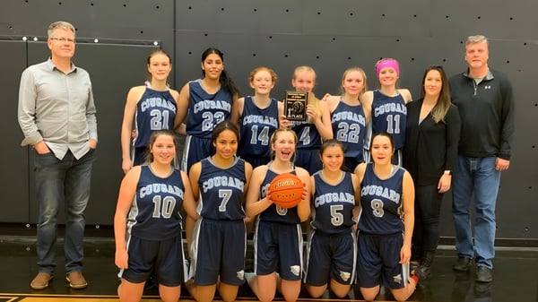 Eine Gruppe junger Basketballspielerinnen in Uniform steht gemeinsam in der Turnhalle der College Heights Secondary School.