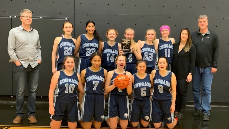Eine Gruppe junger Basketballspielerinnen in Uniform steht gemeinsam in der Turnhalle der College Heights Secondary School.