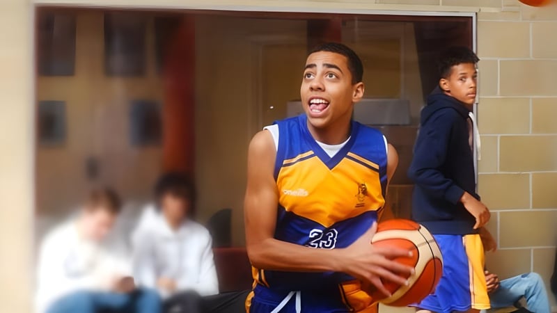 Ein Schüler des College of Richard Collyer hält einen Basketball in einer Sporthalle mit weiteren Personen im Hintergrund.