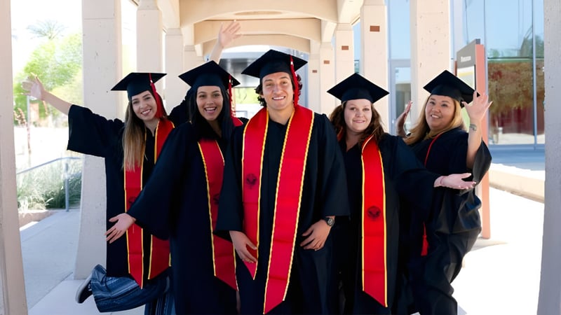 Fünf Absolventinnen in Talaren stehen vor dem Gebäude des College of the Desert.