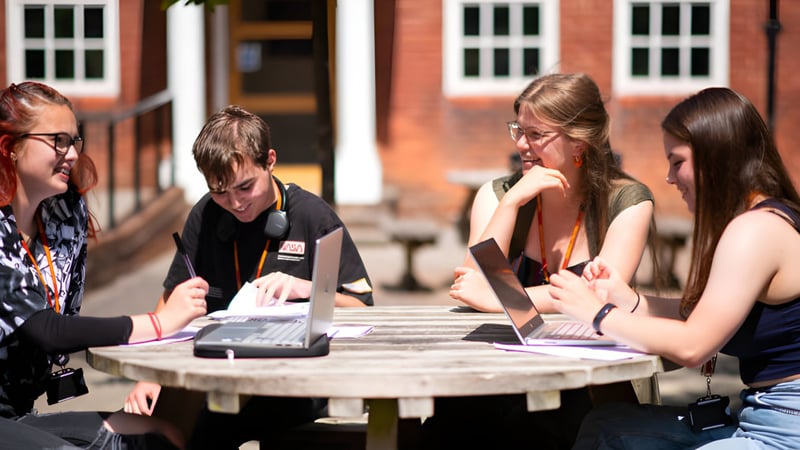 Schüler des College of Richard Collyer diskutieren im Freien an einem Holztisch mit Laptops.