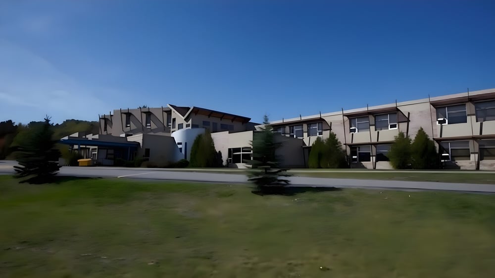 Blick auf den Campus des Collège Sacré-Coeur mit einer Rasenfläche und modernen mehrstöckigen Gebäuden unter blauem Himmel.