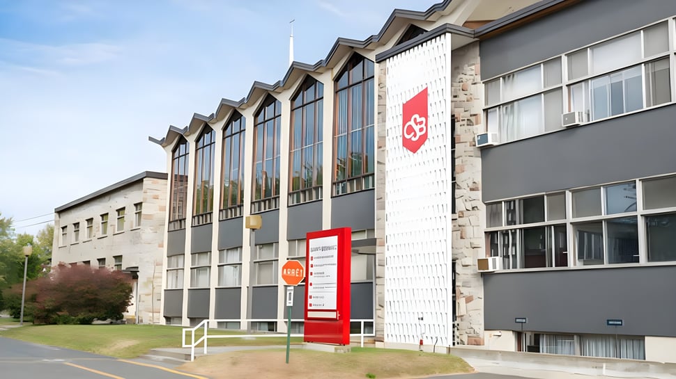 Das mehrstöckige Gebäude mit großen Fenstern und rotem Logo auf dem Campus des College Saint-Bernard ist von einer Grünfläche umgeben.