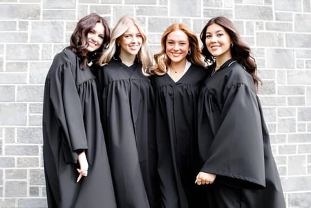 Vier Schülerinnen in schwarzen Abschlussroben stehen vor einer grauen Ziegelwand auf dem Gelände des College Saint-Bernard.