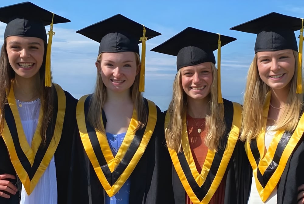 Vier Schülerinnen in Abschlusskleidung stehen vor blauem Himmel auf dem Campus des Collingwood Collegiate Institute.