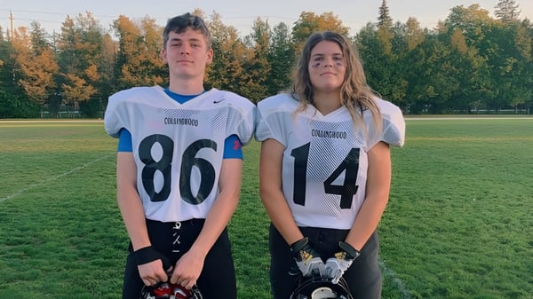 Zwei Schüler des Collingwood Collegiate Institute stehen in Sporttrikots auf einer Wiese mit Wald im Hintergrund.