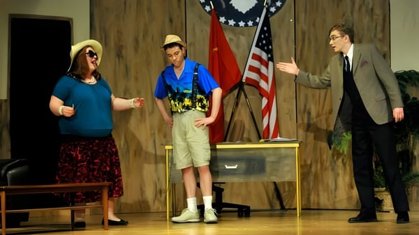 Drei Personen stehen vor einer Holzverkleidung mit amerikanischer Flagge in einer Präsentation an der Colonel By Secondary School.