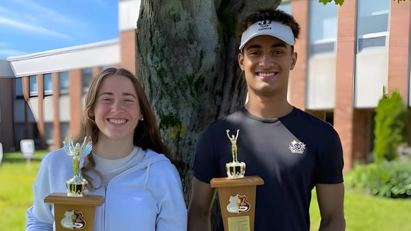 Zwei Personen stehen vor einem Baum auf dem Campus der Colonel Gray High School und halten Trophäen in der Hand.