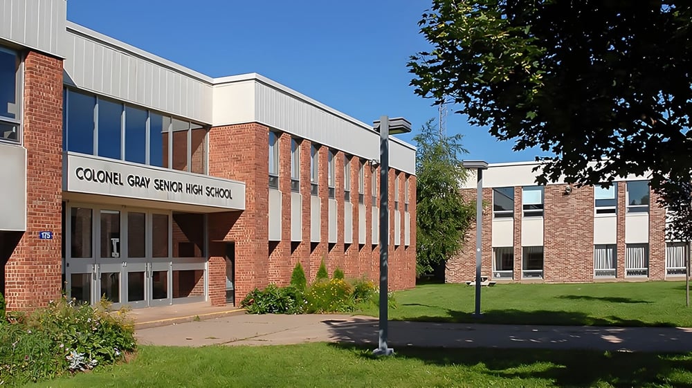 Das mehrstöckige Backsteingebäude der Colonel Gray High School mit großen Fenstern und einer Rasenfläche im Vordergrund.