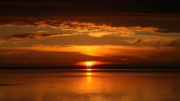 Ein Sonnenuntergang mit orangefarbenem Himmel spiegelt sich ruhig auf dem Wasser nahe der Colonel Gray High School.