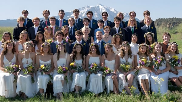 Eine große Gruppe von Schülerinnen und Schülern in formeller Kleidung steht vor einer verschneiten Bergkulisse auf dem Gelände der Colorado Rocky Mountain School.