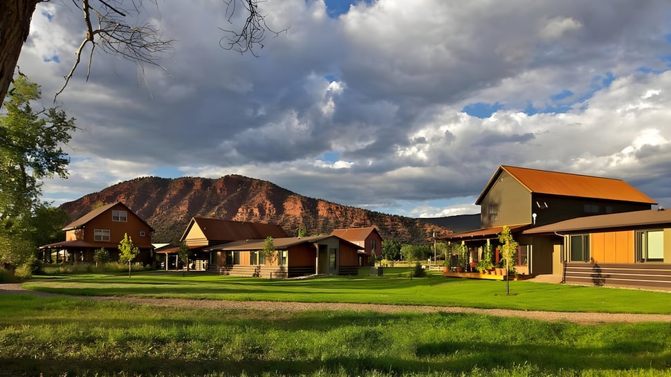 Rustikale Hütten in einer ländlichen Landschaft mit grasbewachsenem Feld und Bergen im Hintergrund auf dem Gelände der Colorado Rocky Mountain School.