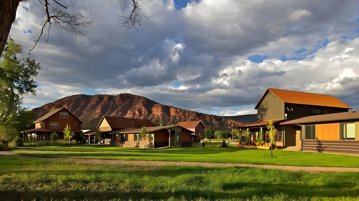 Rustikale Lodges auf einer grünen Wiese mit Bergen im Hintergrund auf dem Gelände der Colorado Rocky Mountain School.