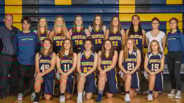 Eine Gruppe junger Basketballspielerinnen posiert vor buntem gelb-blauem Hintergrund auf dem Gelände der Colorado Springs Christian School.