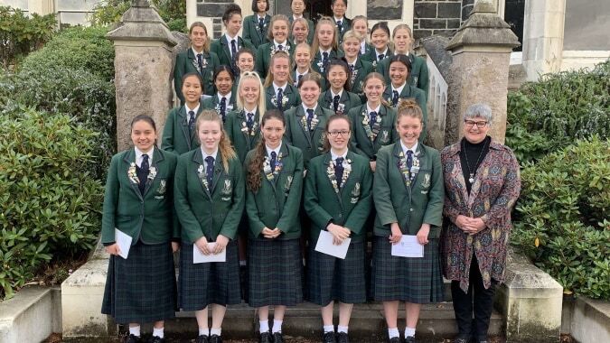 Eine Gruppe von Schülerinnen in Schuluniformen steht vor einem Steingebäude auf dem Campus des Columba College.