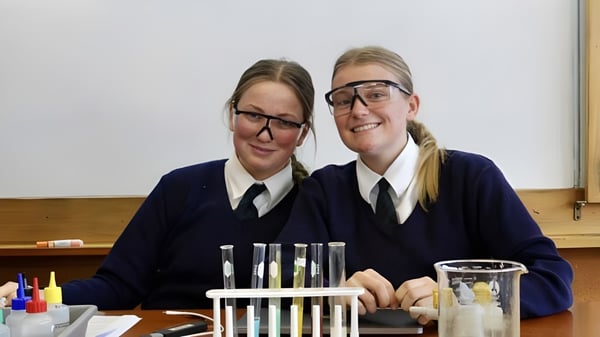 Zwei Schülerinnen in Schuluniformen lächeln gemeinsam in einem Klassenraum auf dem Campus des Columba College.