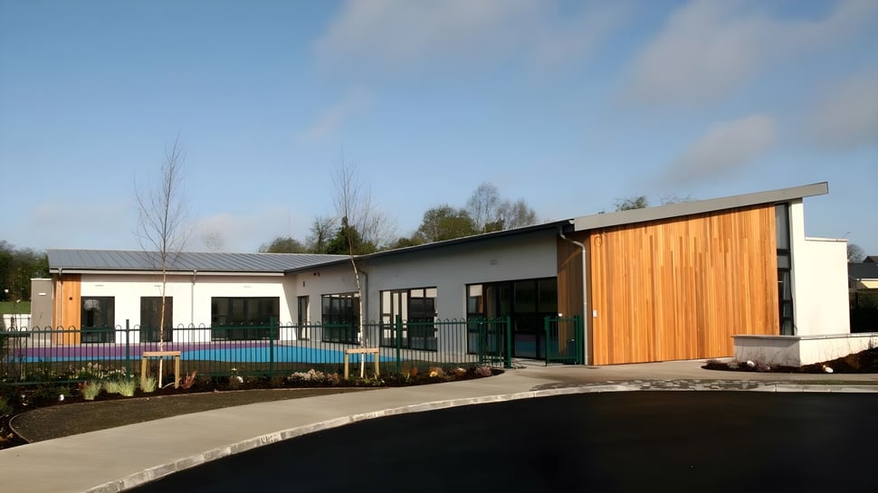 Das moderne eingeschossige Schulgebäude des Columba College steht neben einem Schwimmbecken in einer gepflegten Außenanlage.