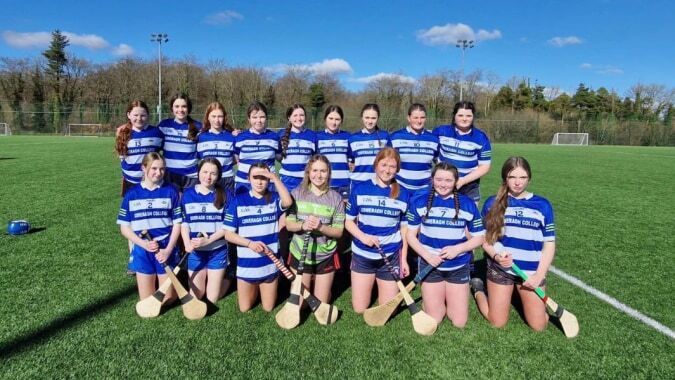 Eine Gruppe junger Sportlerinnen der Comeragh College posiert gemeinsam auf dem Fußballfeld.