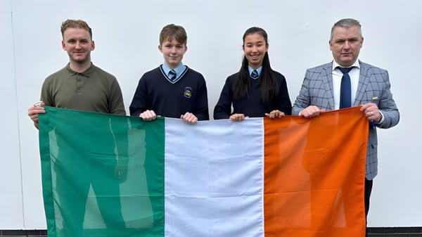 Vier Personen halten die irische Flagge vor weißem Hintergrund auf dem Campus des Comeragh College.
