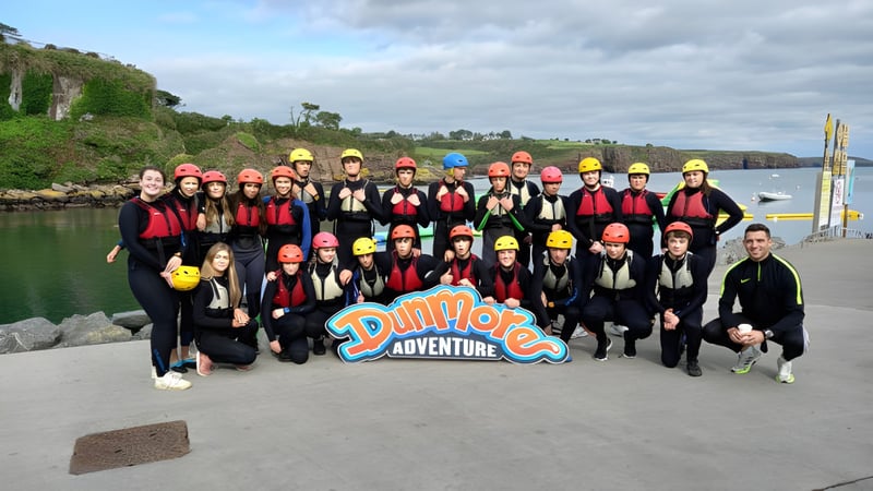 Eine Gruppe von Schülern des Comeragh College posiert vor einer Landschaft mit Klippen, Wasser und Vegetation.