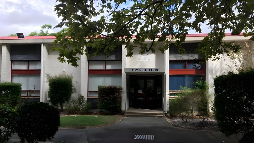 Das Verwaltungsgebäude mit rotem Dach und Eingangsbereich auf dem Campus des Como Secondary College ist von Bäumen umgeben.