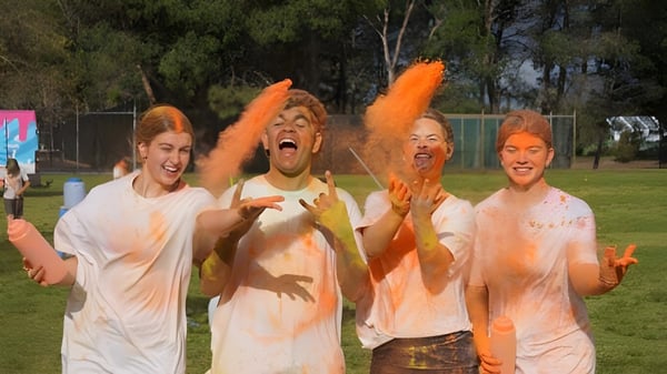 Schüler des Como Secondary College werfen im Freien orangefarbenes Pulver in die Luft bei einer Veranstaltung.
