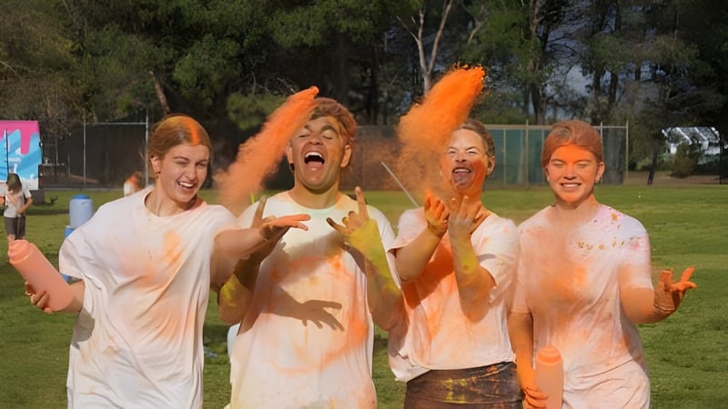 Schüler des Como Secondary College werfen im Freien orangefarbenes Pulver in die Luft bei einer Veranstaltung.