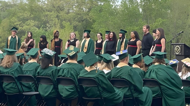 Eine Gruppe Abiturienten der Comstock Park High School steht draußen in grünen Talaren umgeben von Bäumen.