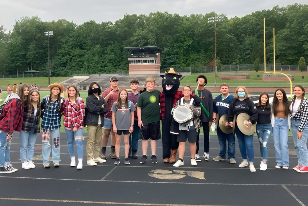 Eine Gruppe von Schülerinnen und Schülern steht auf dem Sportplatz der Comstock Park High School neben Sportgeräten und Bäumen.