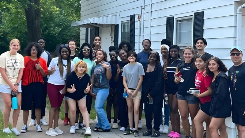 Eine Gruppe von Schülerinnen und Schülern steht vor dem Gebäude der Connecticut IB Academy mit grüner Umgebung im Hintergrund.