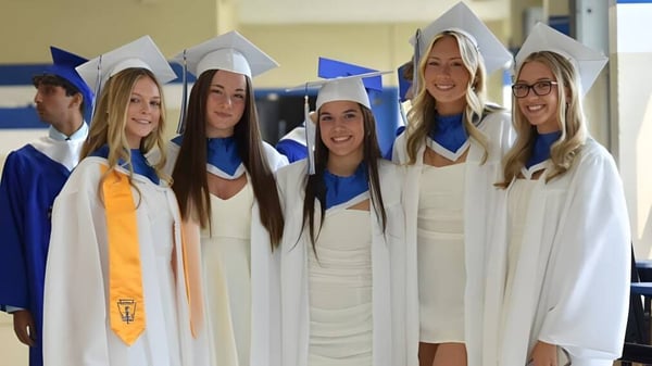 Eine Gruppe Schülerinnen der Conwell-Egan Catholic High School steht in weißen Abschlusskleidern und Mützen zusammen und posiert für ein Foto.