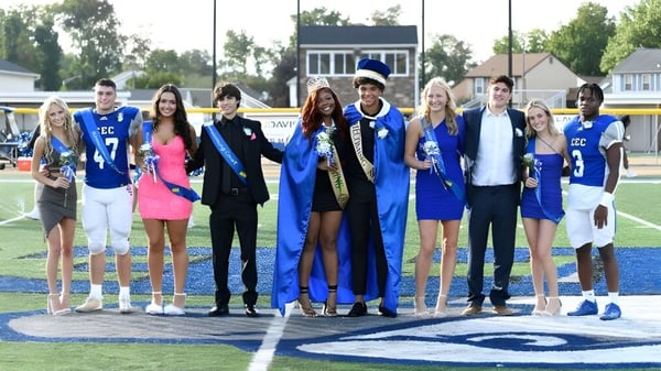 Eine Gruppe von Absolventinnen und Absolventen der Conwell-Egan Catholic High School steht auf einem Sportfeld mit Gebäuden und Bäumen im Hintergrund.