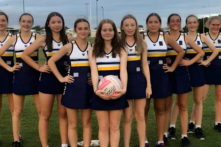 Eine Gruppe junger Sportlerinnen steht zusammen auf dem Sportfeld der Coolum State High School unter bewölktem Himmel.
